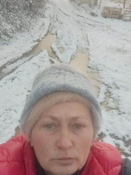 Person in a red jacket wearing a gray knit hat takes a selfie on a snowy, muddy trail.