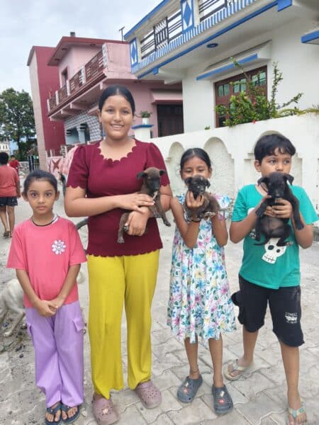 Four children standing on a street, each holding a small brown puppy.